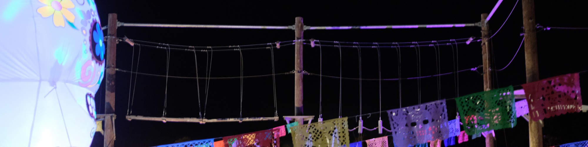 Neon Heights high ropes aerial adventure course glowing with neon lights, featuring zip lines, wobbly bridges, swingy steps, and a thrilling 70-metre zip wire descent under the night sky.