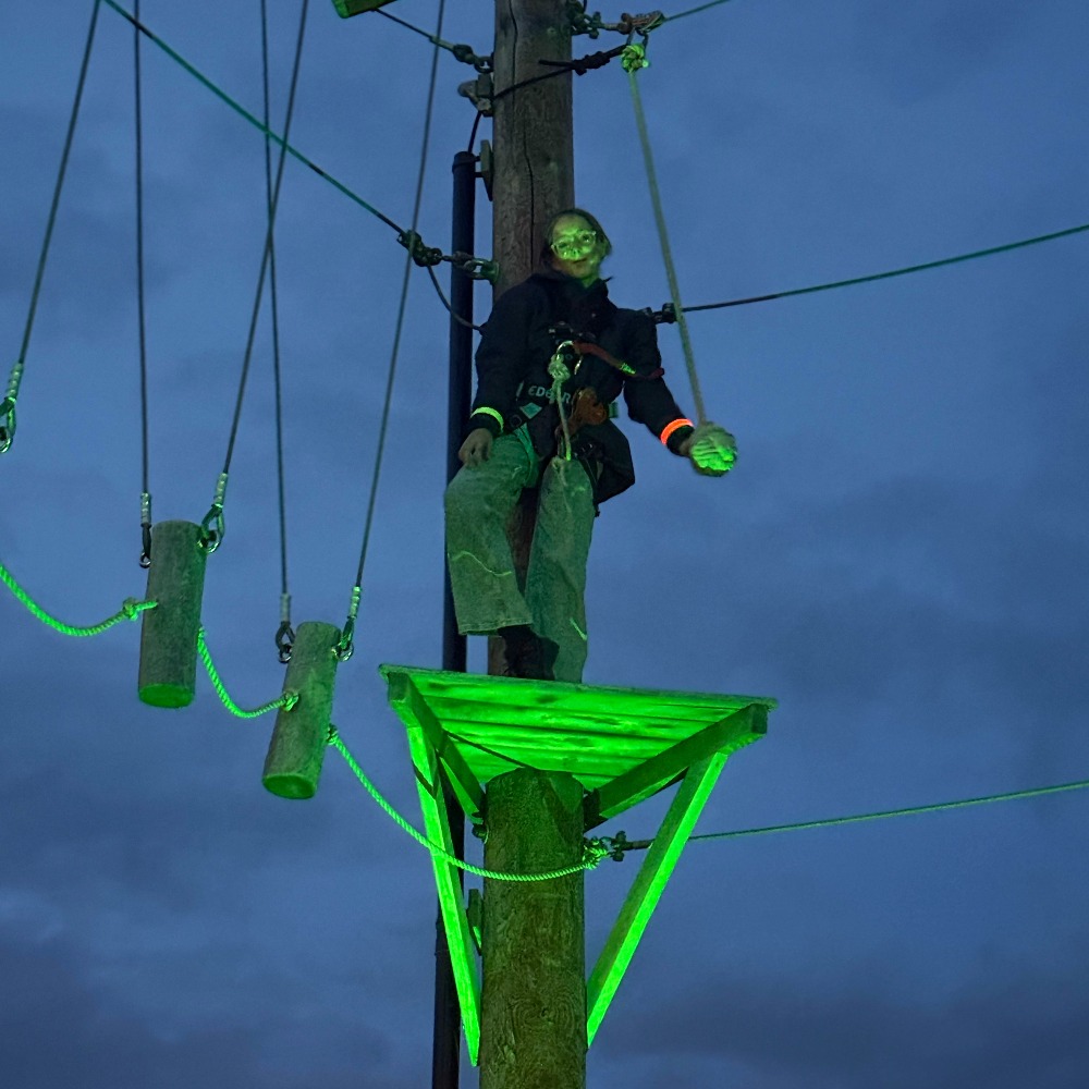 Neon Heights high ropes aerial adventure course glowing with neon lights, featuring zip lines, wobbly bridges, swingy steps, and a thrilling 70-metre zip wire descent under the night sky.
