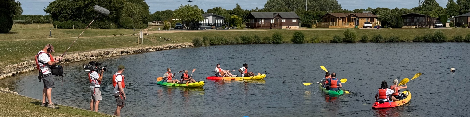 Four in a Bed contestants kayaking on the lake at Aztec Adventure Lower Moor, while filmed by the Channel 4 crew