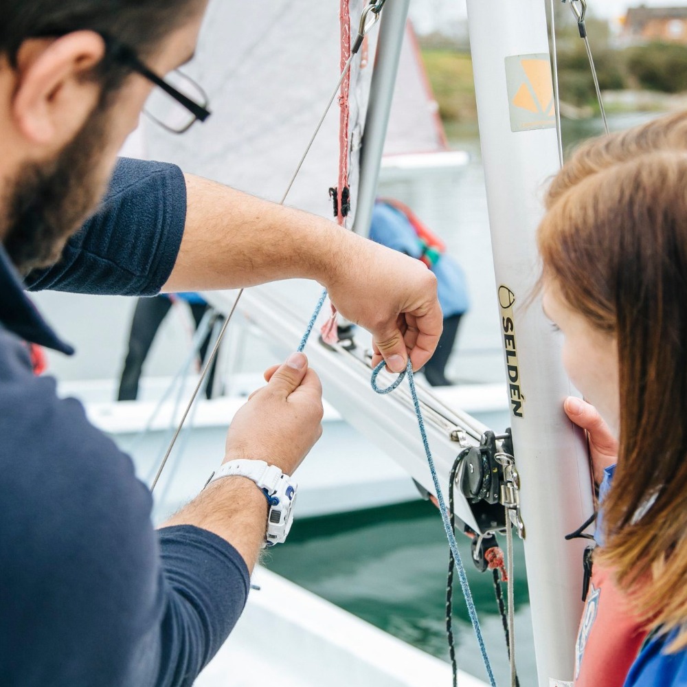 Sailing instructor showing a young sailor how to rig a dinghy mast on an RYA Youth Sailing course at Aztec Adventure Upton Warren