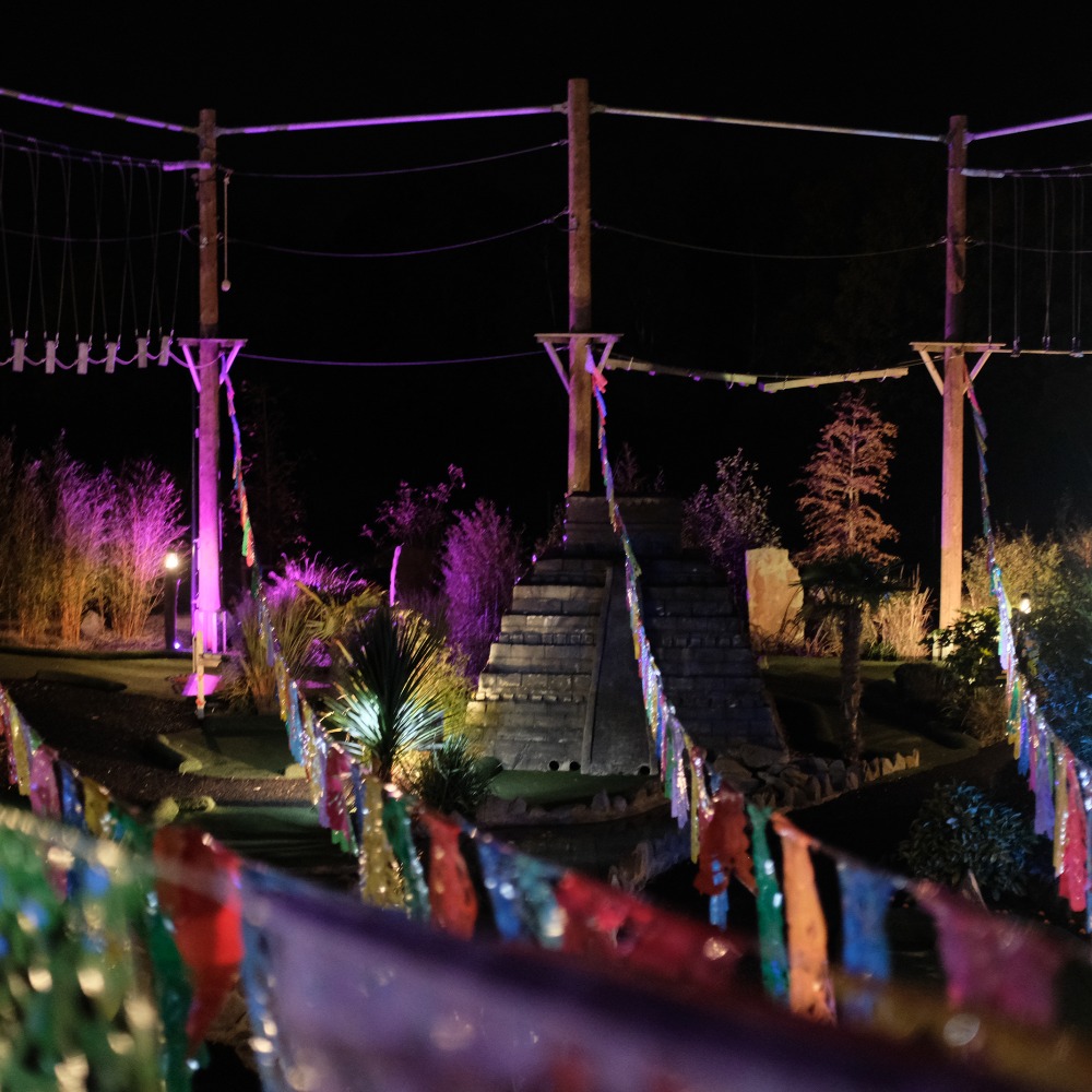 Neon Heights high ropes aerial adventure course glowing with neon lights, featuring zip lines, wobbly bridges, swingy steps, and a thrilling 70-metre zip wire descent under the night sky.