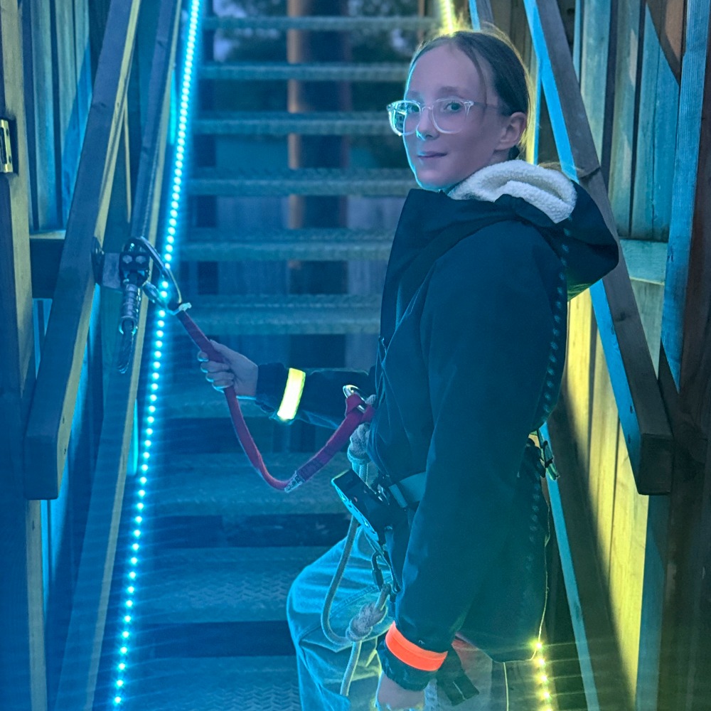 Neon Heights high ropes aerial adventure course glowing with neon lights, featuring zip lines, wobbly bridges, swingy steps, and a thrilling 70-metre zip wire descent under the night sky.